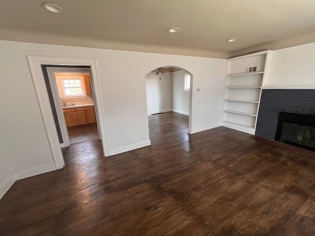 unfurnished living room featuring arched walkways, dark wood-style flooring, a fireplace, and baseboards