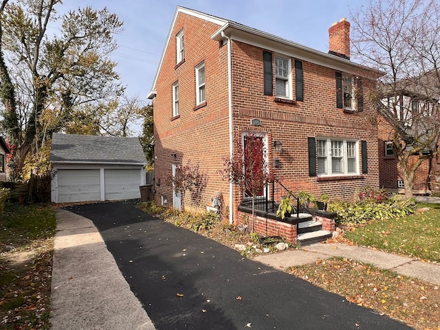 view of front of home featuring a garage, brick siding, a chimney, and an outdoor structure