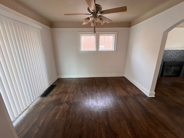 empty room featuring dark wood-style floors, arched walkways, visible vents, a brick fireplace, and baseboards