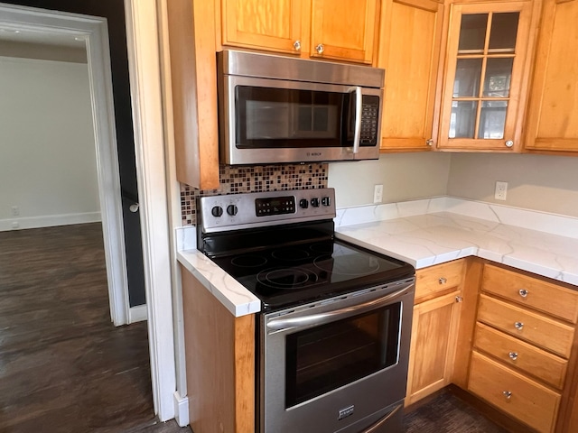 kitchen with brown cabinetry, glass insert cabinets, stainless steel appliances, and light stone counters