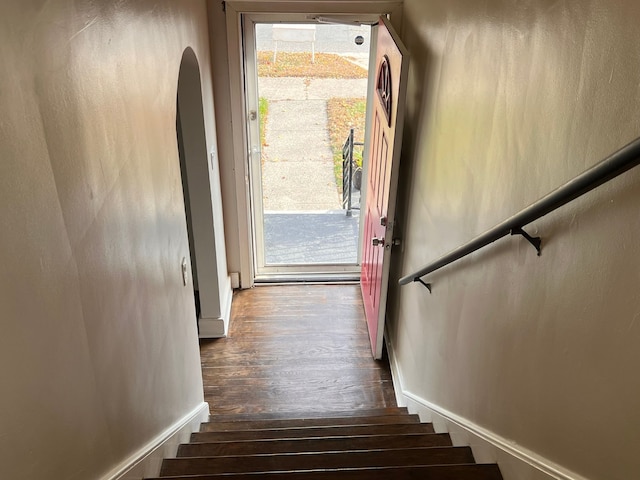 stairway featuring baseboards, arched walkways, and wood finished floors