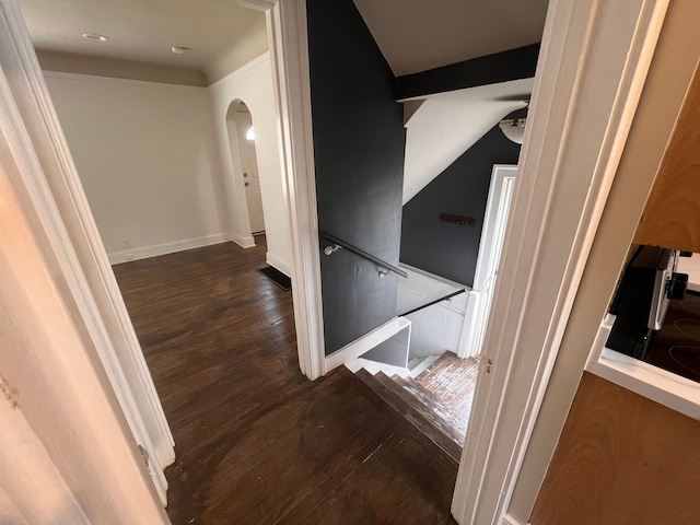 corridor featuring arched walkways, dark wood-style flooring, baseboards, and an upstairs landing