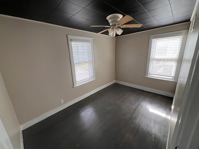 spare room featuring baseboards, dark wood-type flooring, a ceiling fan, and a healthy amount of sunlight