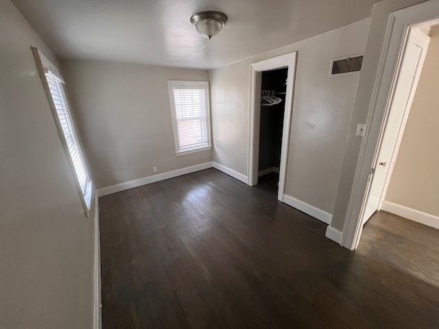 unfurnished bedroom featuring dark wood-type flooring, a closet, visible vents, and baseboards