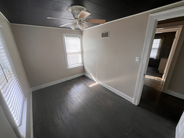 empty room with dark wood-style floors, visible vents, ceiling fan, and baseboards