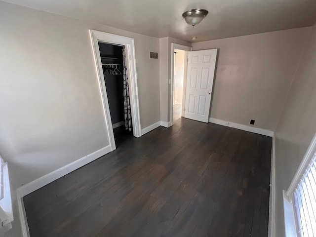 unfurnished bedroom with dark wood-style flooring, a closet, visible vents, and baseboards