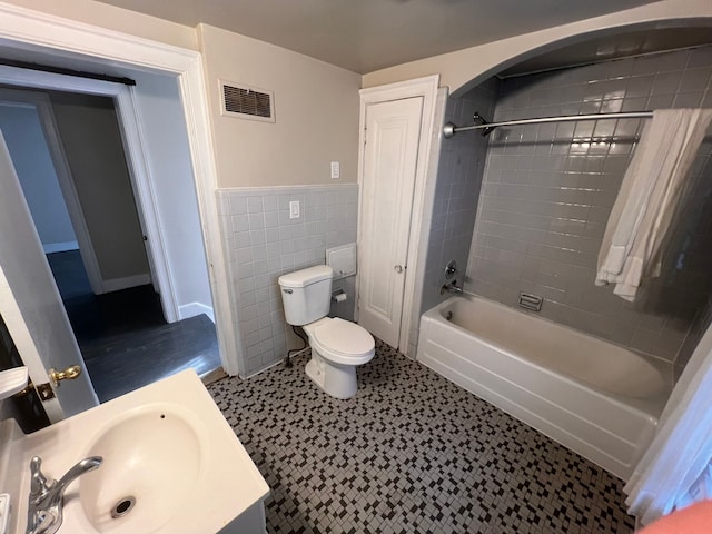 bathroom featuring a wainscoted wall, tile walls, visible vents, toilet, and tub / shower combination