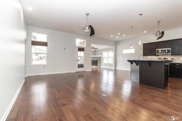 kitchen with dark wood finished floors, ceiling fan, stainless steel microwave, open floor plan, and a kitchen breakfast bar