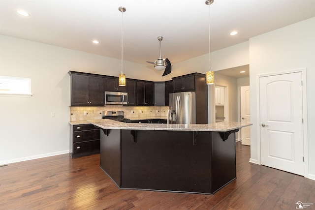 kitchen with dark wood-style floors, light stone counters, stainless steel appliances, tasteful backsplash, and a kitchen breakfast bar