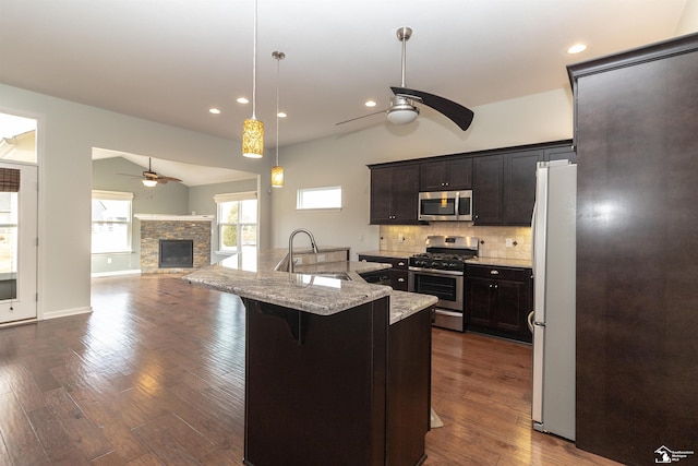 kitchen featuring a sink, a ceiling fan, appliances with stainless steel finishes, backsplash, and a kitchen bar