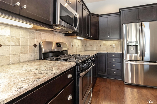 kitchen with stainless steel appliances, dark wood-style flooring, backsplash, and light stone countertops