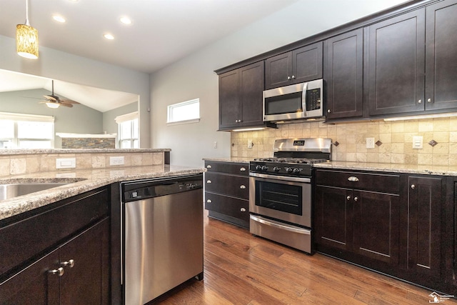 kitchen with lofted ceiling, appliances with stainless steel finishes, decorative backsplash, light stone countertops, and dark wood-style floors