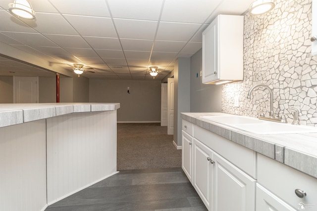 kitchen featuring dark wood finished floors, light countertops, white cabinets, a sink, and a drop ceiling