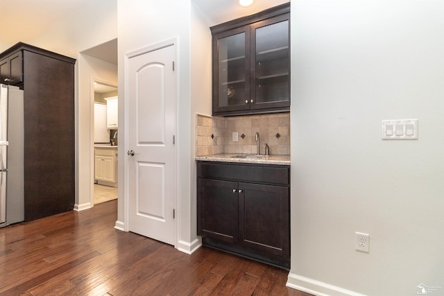 bar with baseboards, dark wood-type flooring, freestanding refrigerator, a sink, and backsplash