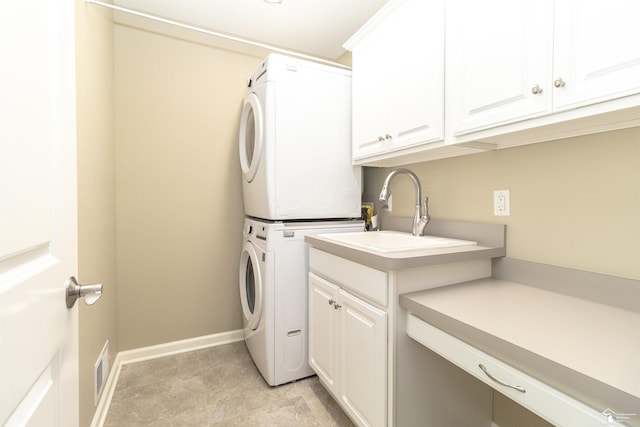 clothes washing area with cabinet space, visible vents, baseboards, stacked washer and clothes dryer, and a sink