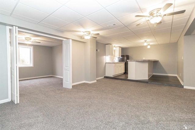 basement with a paneled ceiling, baseboards, dark carpet, and freestanding refrigerator