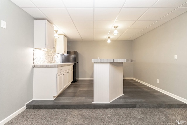 kitchen with backsplash, freestanding refrigerator, white cabinets, a drop ceiling, and baseboards