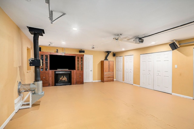 interior space featuring a wood stove, ceiling fan, baseboards, and concrete flooring