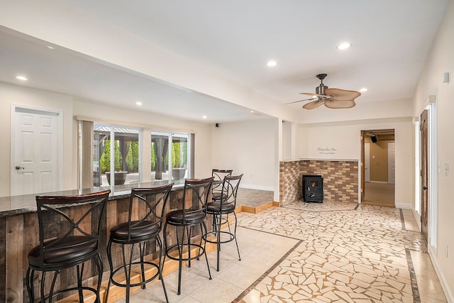 interior space with baseboards, a ceiling fan, a wood stove, a kitchen bar, and recessed lighting