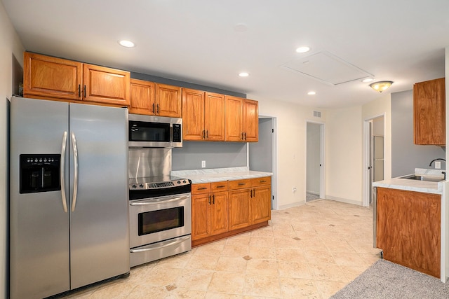 kitchen with brown cabinets, appliances with stainless steel finishes, light countertops, and a sink