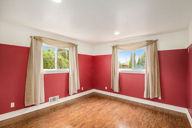 empty room featuring a wealth of natural light, wood finished floors, visible vents, and baseboards