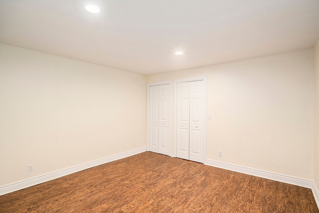 unfurnished bedroom with wood finished floors, two closets, and baseboards