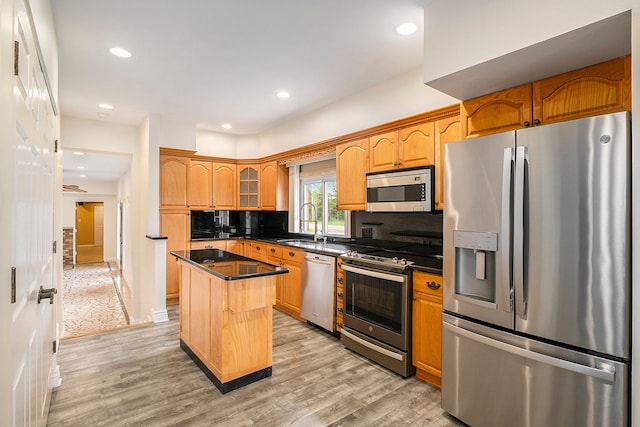 kitchen featuring a sink, a kitchen island, light wood-style floors, appliances with stainless steel finishes, and dark countertops