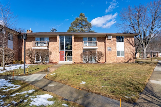 view of front of property featuring a balcony, a chimney, a front lawn, and brick siding