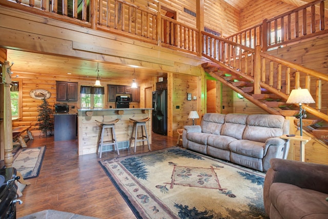 living area with wooden walls, stairway, dark wood-style flooring, a high ceiling, and log walls