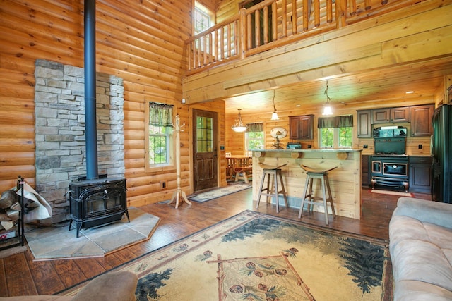 living room featuring a wealth of natural light, rustic walls, dark wood finished floors, and a wood stove