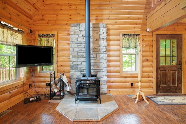 living area featuring a wood stove, high vaulted ceiling, log walls, and wood finished floors