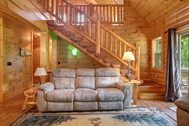 living room with high vaulted ceiling, wood finished floors, wooden walls, and stairs