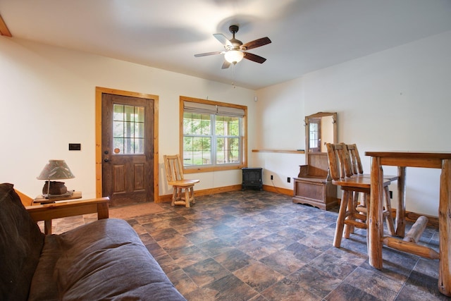 interior space featuring stone finish flooring, ceiling fan, a wood stove, and baseboards