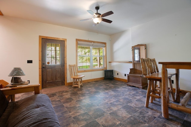 entryway featuring a ceiling fan, a wood stove, stone finish floor, and baseboards