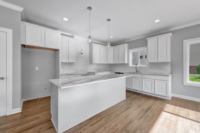 kitchen featuring hanging light fixtures, white cabinetry, a kitchen island, a sink, and light wood-type flooring