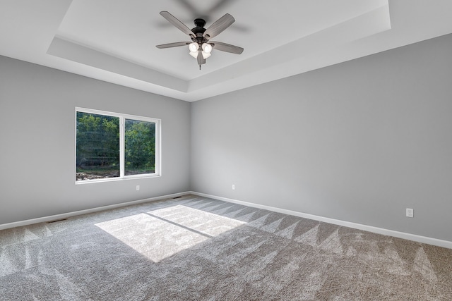 carpeted empty room featuring a tray ceiling, visible vents, ceiling fan, and baseboards