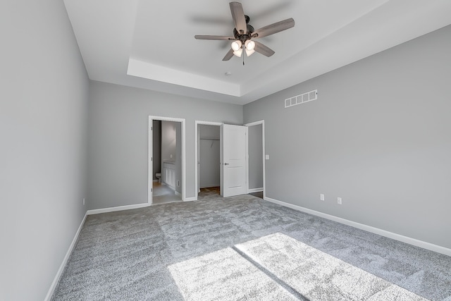 unfurnished bedroom featuring a tray ceiling, carpet, visible vents, and baseboards