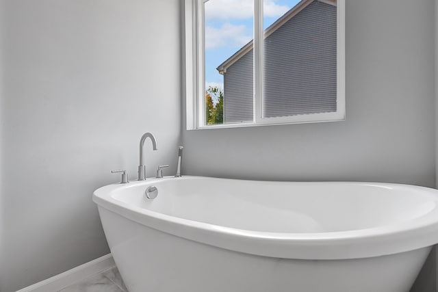 full bath with marble finish floor, a soaking tub, and baseboards