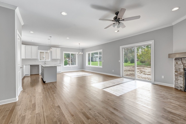 unfurnished living room with light wood-style flooring, ornamental molding, baseboards, and a stone fireplace