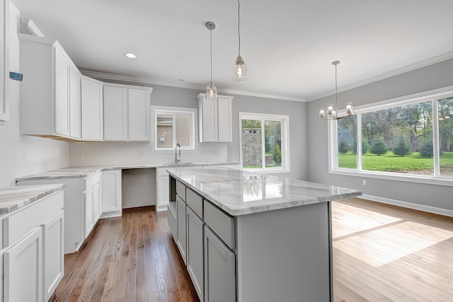 kitchen with decorative light fixtures, light stone counters, white cabinets, and a center island