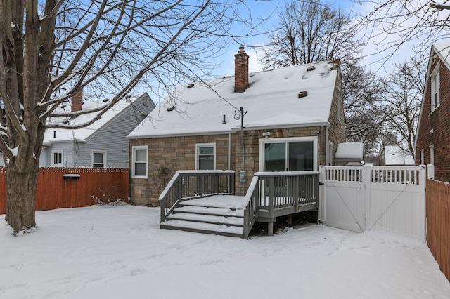 snow covered back of property with stone siding, a gate, a fenced backyard, and a wooden deck