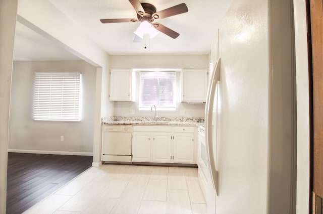 kitchen featuring light stone counters, white cabinets, a sink, white appliances, and baseboards