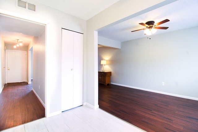 interior space featuring a ceiling fan, visible vents, baseboards, and wood finished floors