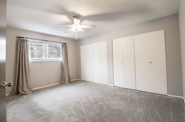 unfurnished bedroom featuring carpet, a textured ceiling, a ceiling fan, and two closets