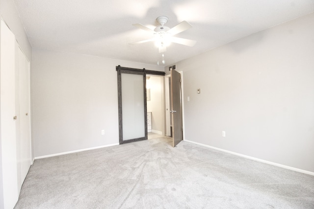 unfurnished bedroom featuring a ceiling fan, light carpet, baseboards, and a barn door