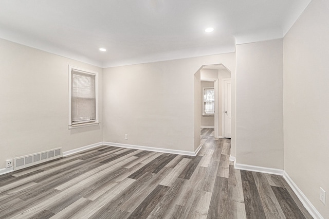 spare room featuring baseboards, visible vents, arched walkways, and dark wood-type flooring