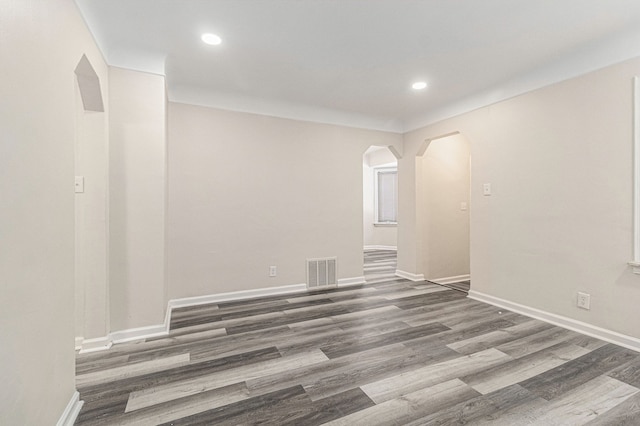 unfurnished room featuring arched walkways, wood finished floors, visible vents, and baseboards