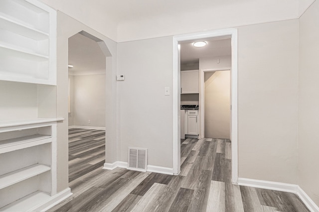 hallway featuring baseboards, visible vents, arched walkways, and wood finished floors