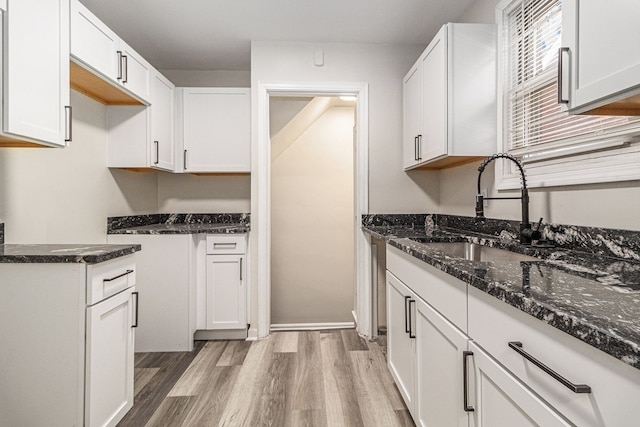 kitchen featuring dark stone countertops, white cabinetry, light wood-style flooring, and a sink