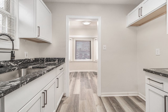 kitchen with baseboards, dark stone counters, light wood-style floors, white cabinetry, and a sink